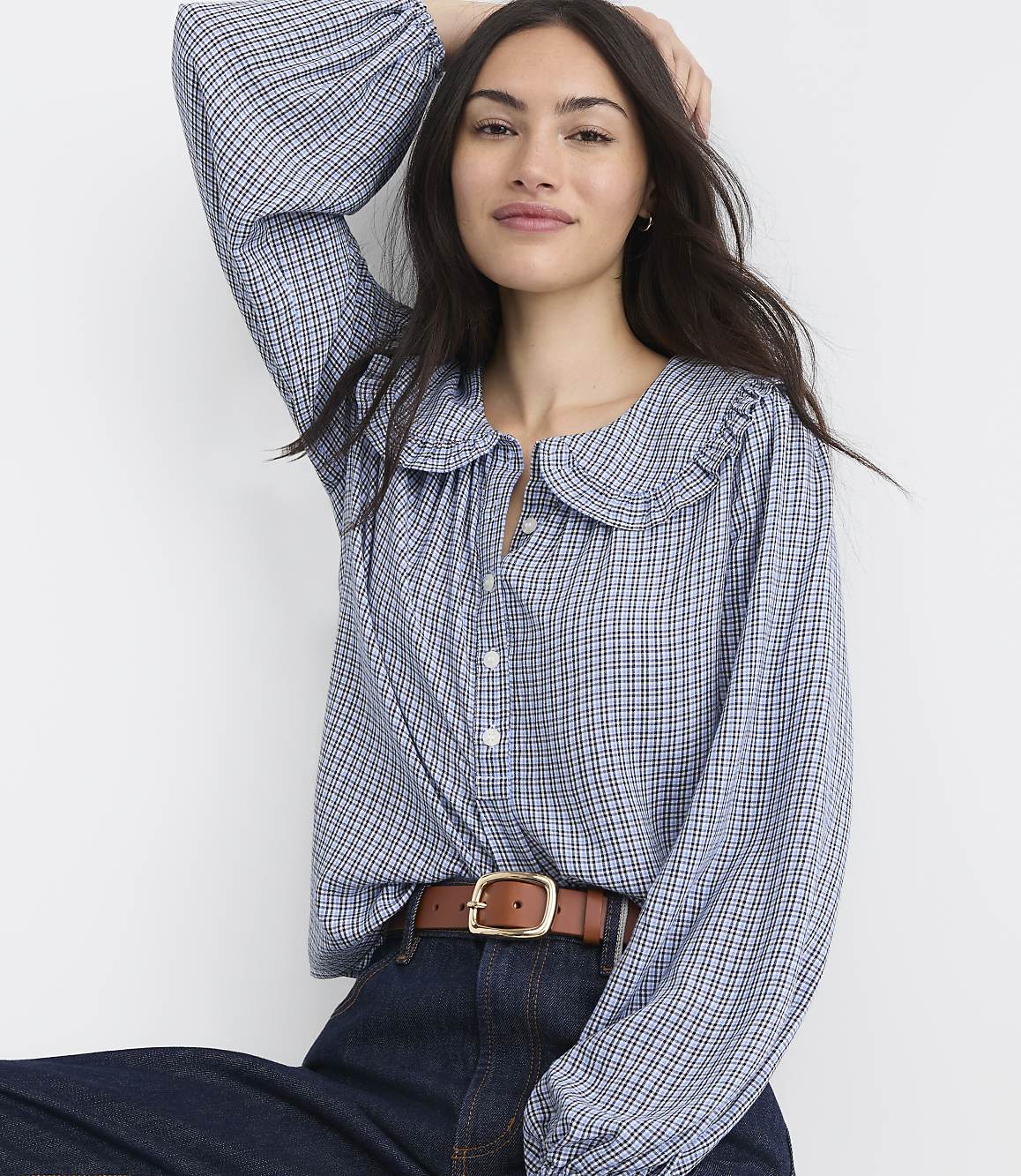 A woman in a blue gingham blouse and brown belt poses against a plain white background.