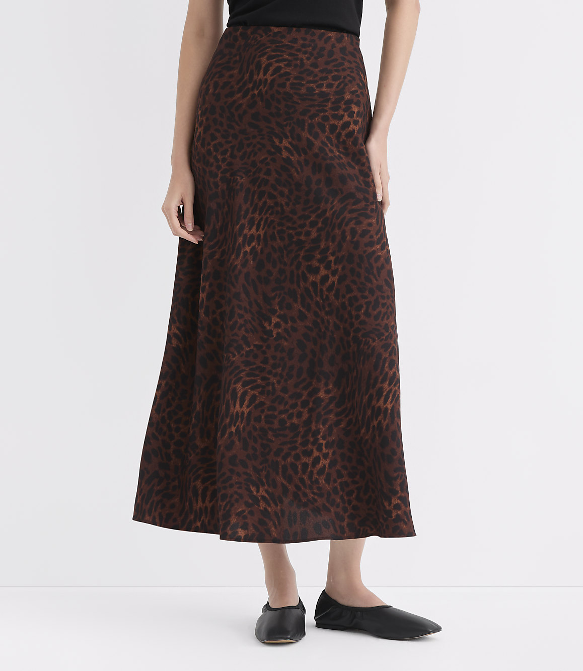 A woman in a leopard print skirt and black flats stands against a plain white background.