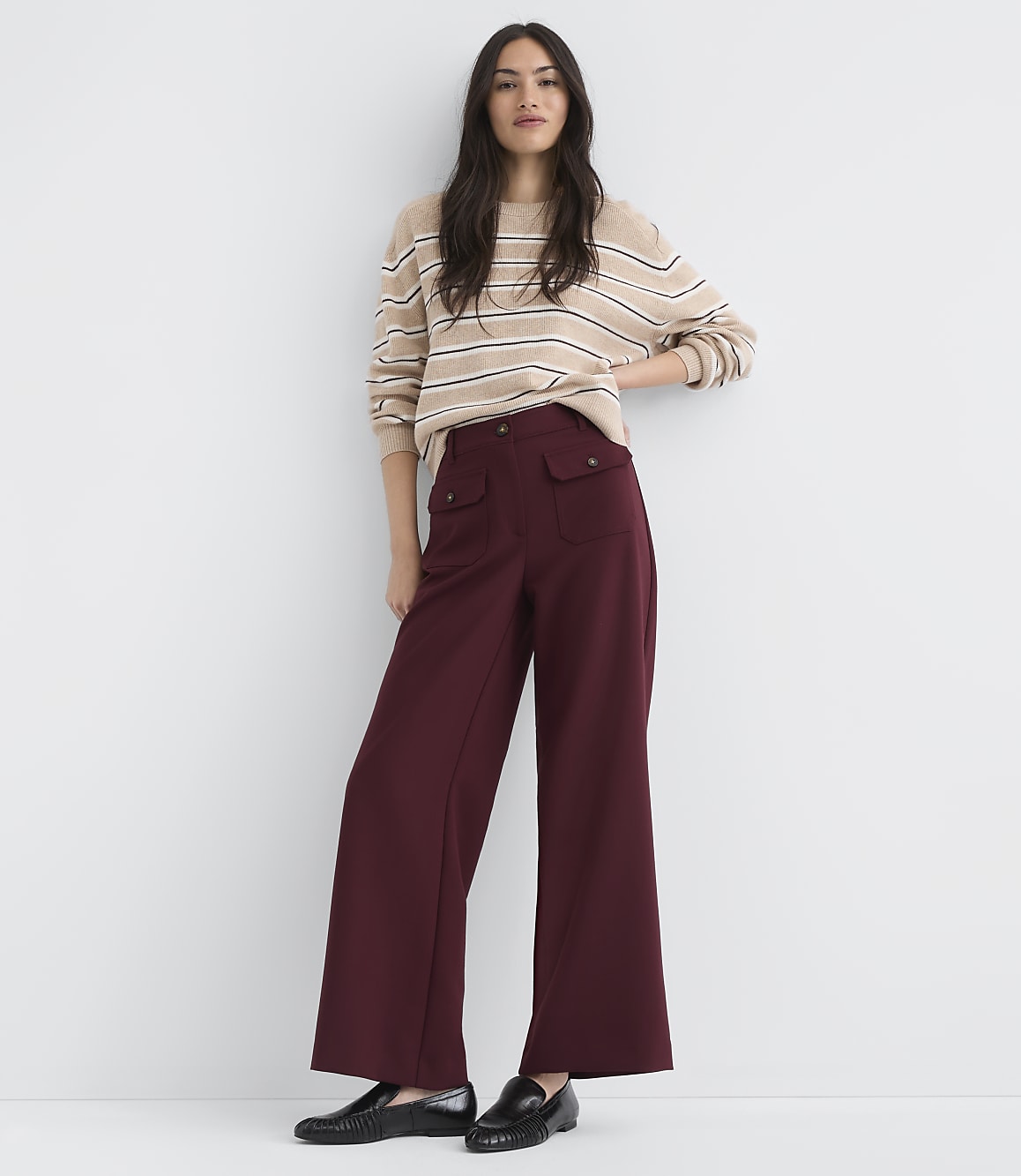 A woman in a striped sweater and maroon wide-leg pants stands against a plain white background.