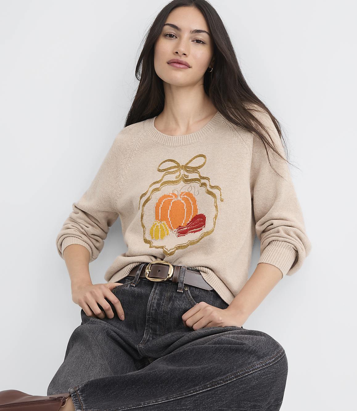 A woman in a beige sweater with a pumpkin design sits in front of a plain light background.