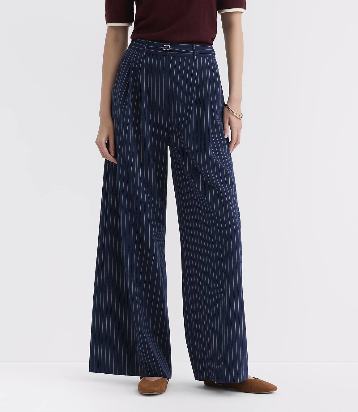A person stands in the foreground wearing navy pinstripe wide-leg pants and brown flats, against a plain white background.
