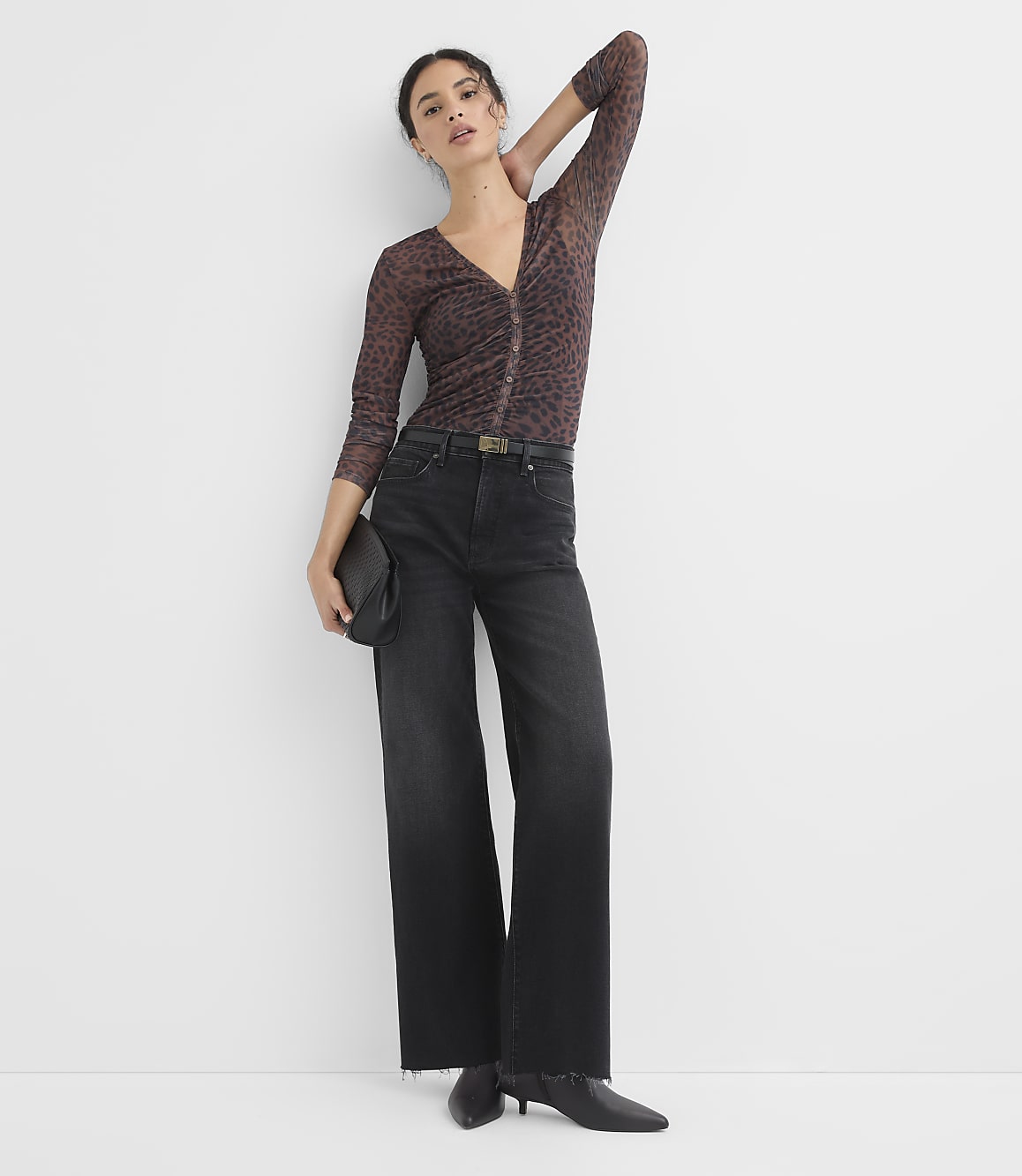 A woman in a sheer animal-print top and wide-leg jeans poses against a plain white background.