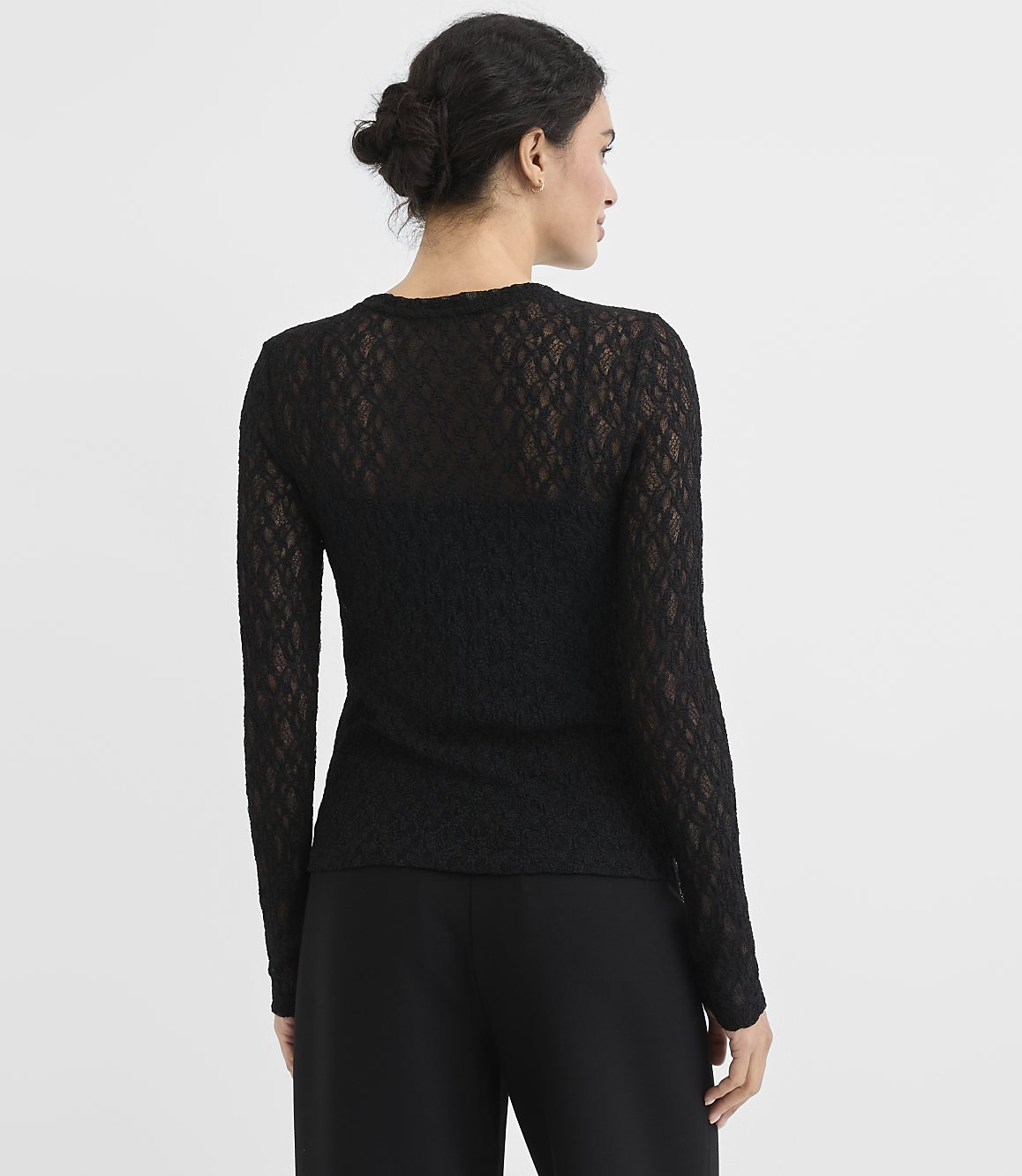A woman in a black lace top and pants stands against a plain white background.