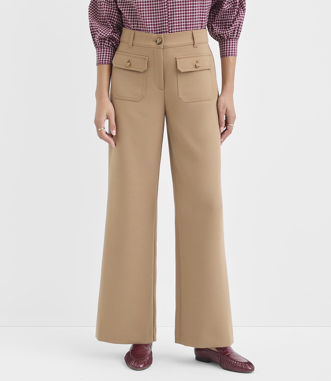 A person in tan wide-leg pants with flap pockets and a patterned blouse stands against a plain white background.