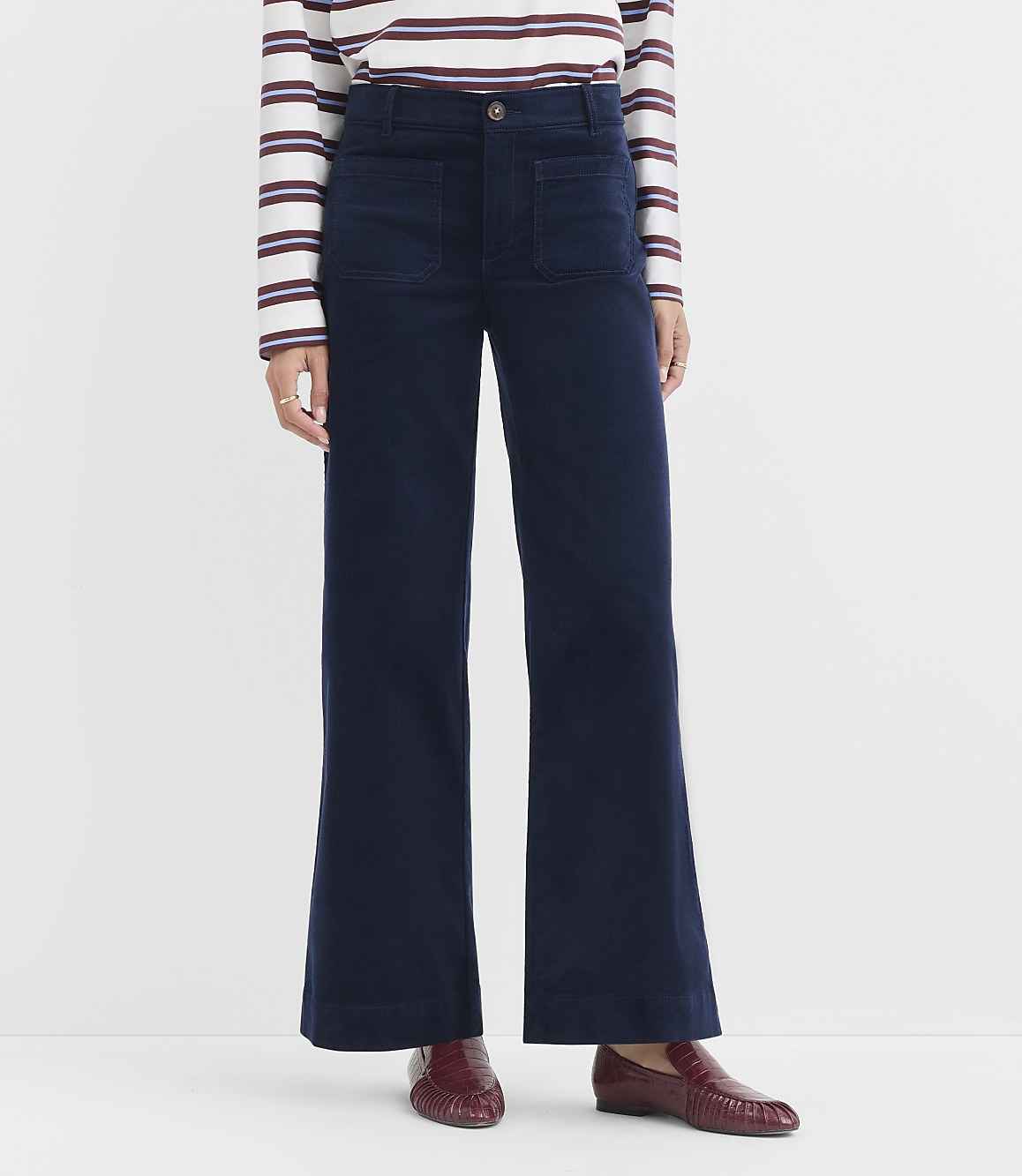 A person wearing navy wide-leg corduroy pants and a striped shirt stands against a plain white background.