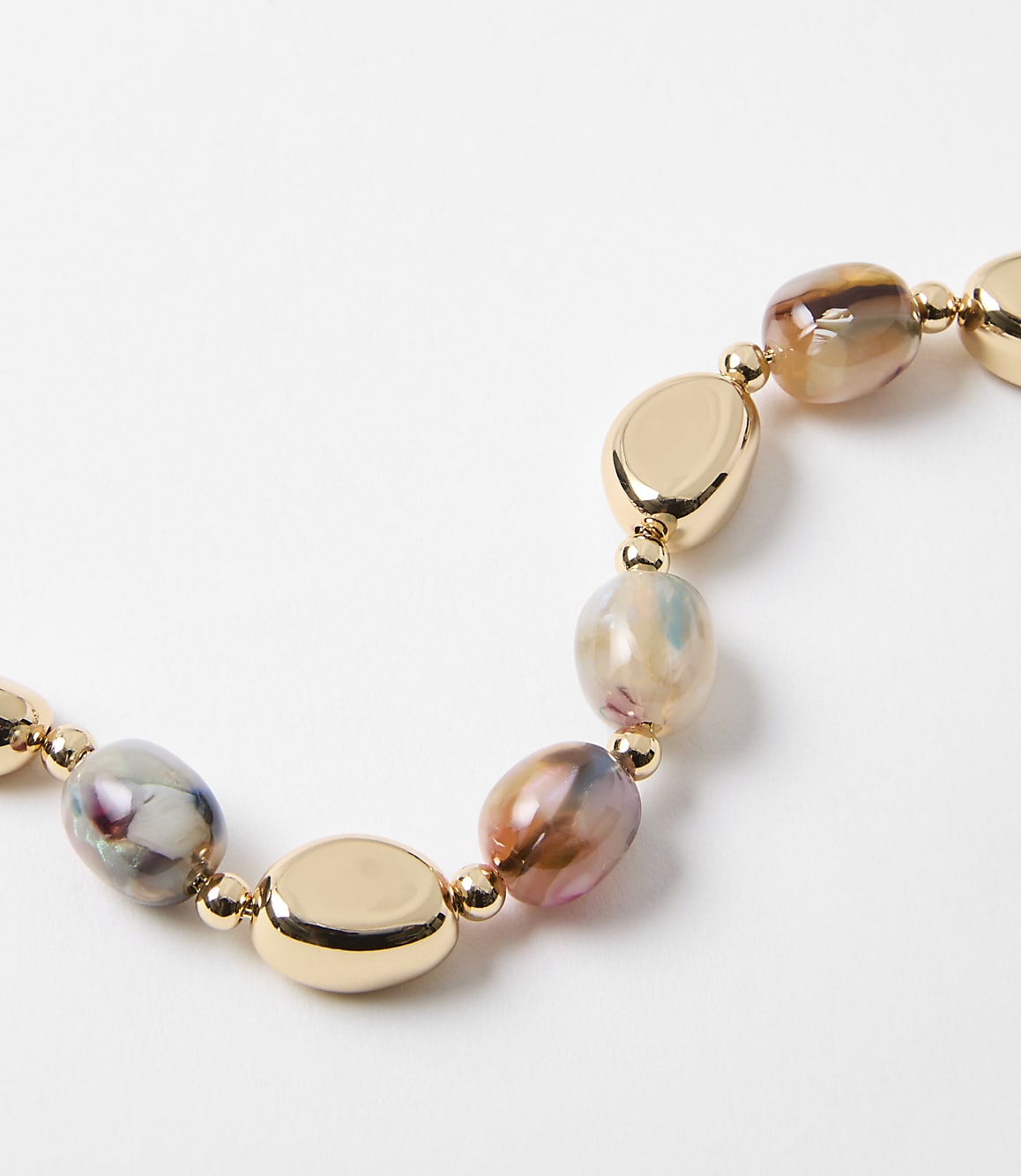 A close-up of a necklace with irregular, marbled beads and gold oval accents rests on a plain white background.