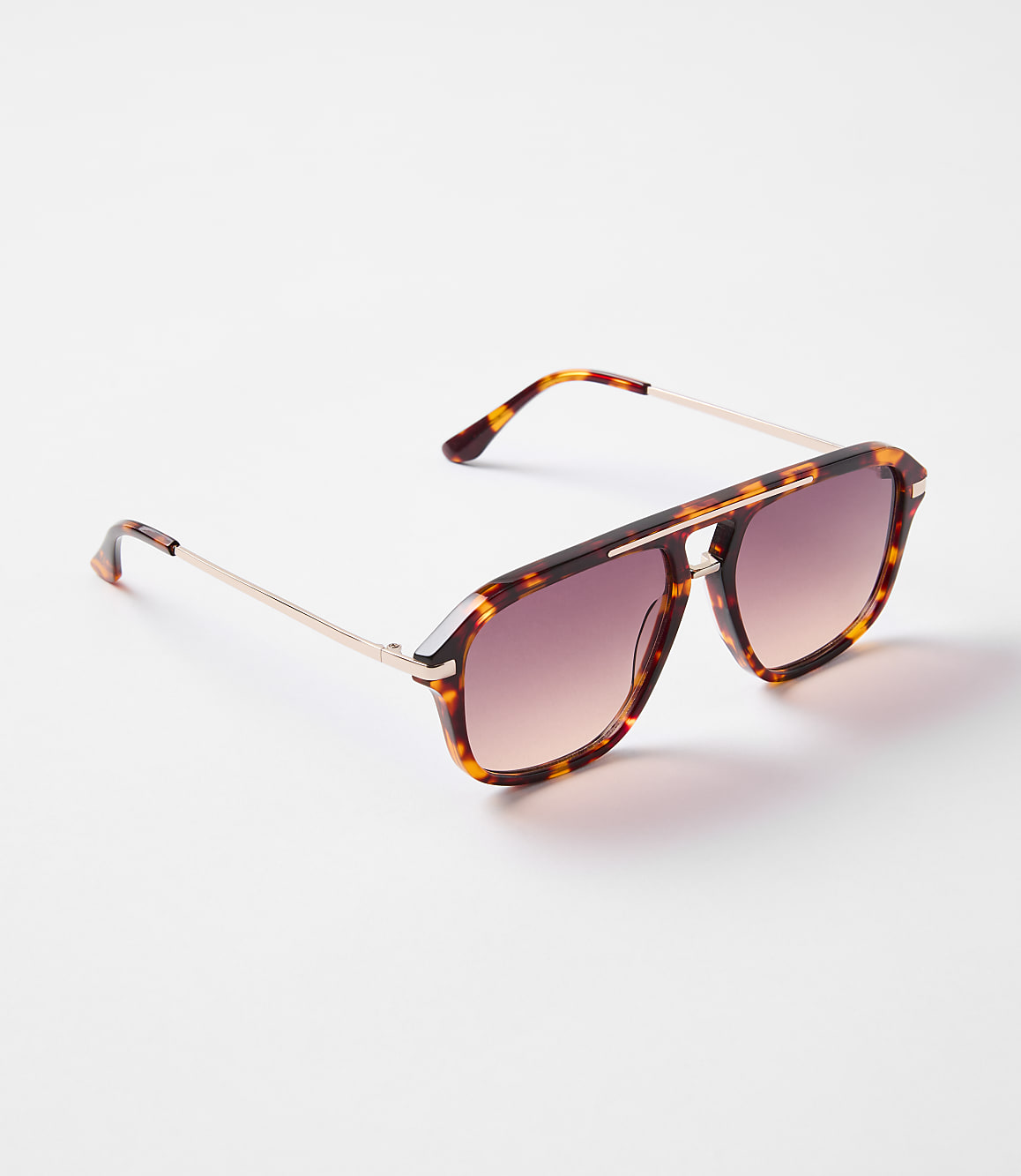 Tortoiseshell aviator sunglasses with rose-tinted lenses rest on a white surface.