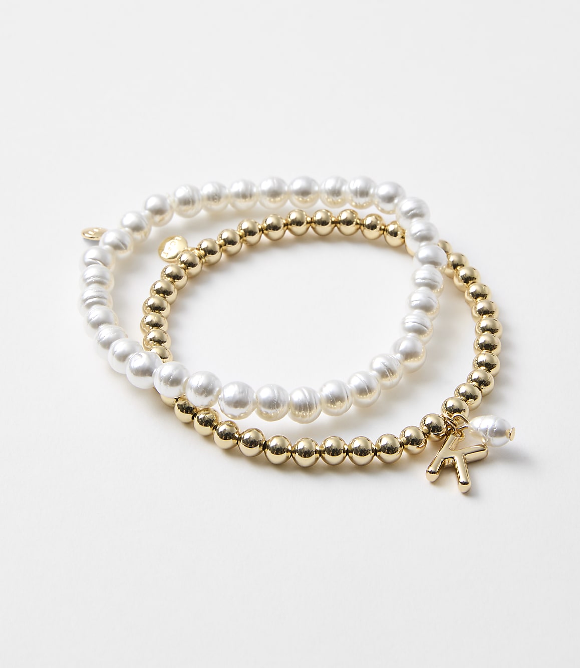 Two bracelets, one with pearls and the other with gold beads and a charm, rest on a plain white background.