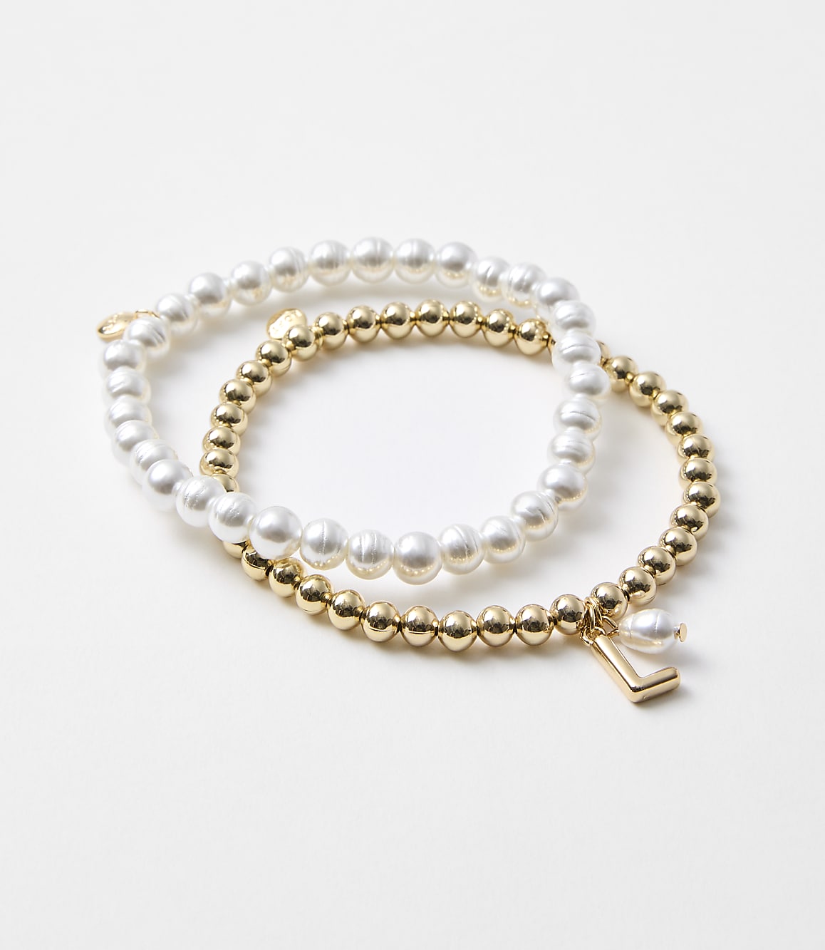Two bracelets, one with pearls and the other with gold beads and a charm, rest on a plain white background.