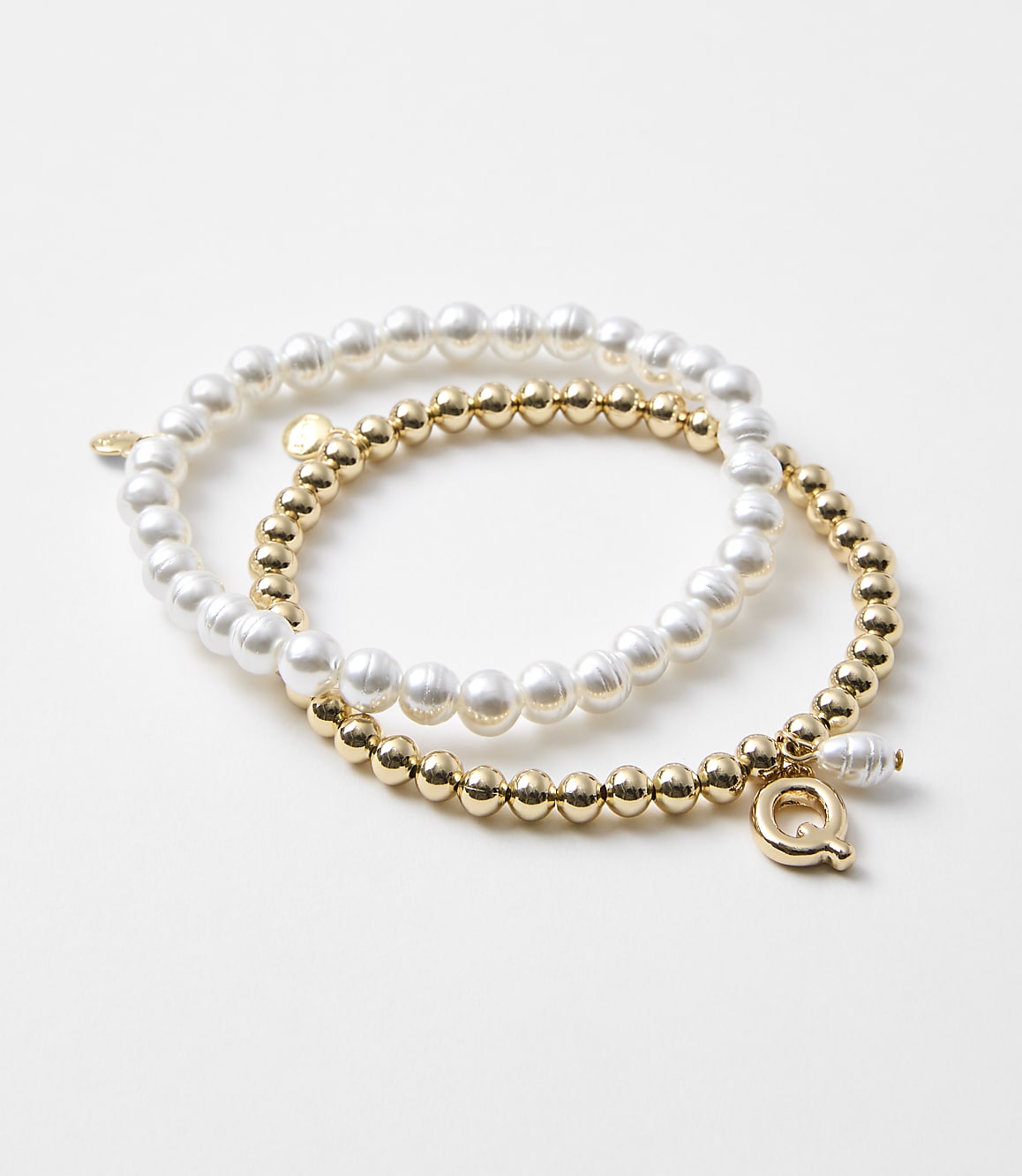 Two bracelets, one with pearls and the other with gold beads, rest on a plain white background.