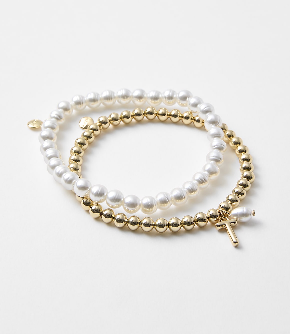 Two bracelets, one with pearls and the other with gold beads and a cross charm, rest on a plain white background.