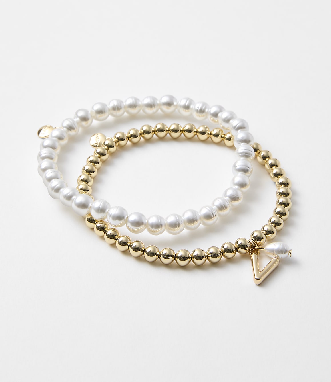 Two bracelets, one with pearls and the other with gold beads and a triangle charm, rest on a plain white background.