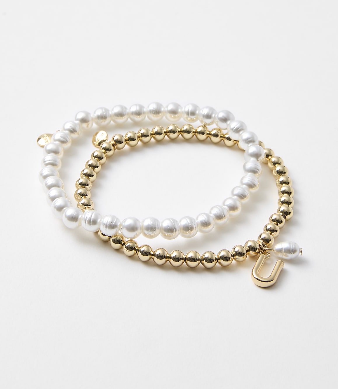 Two bracelets, one with pearls and the other with gold beads and a charm, rest on a plain white background.