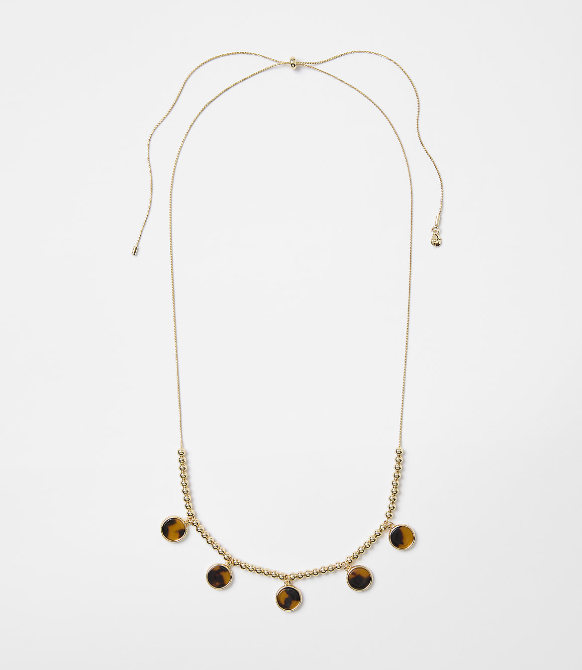A delicate gold necklace with small beads and tortoise shell pendants hangs against a plain white background.