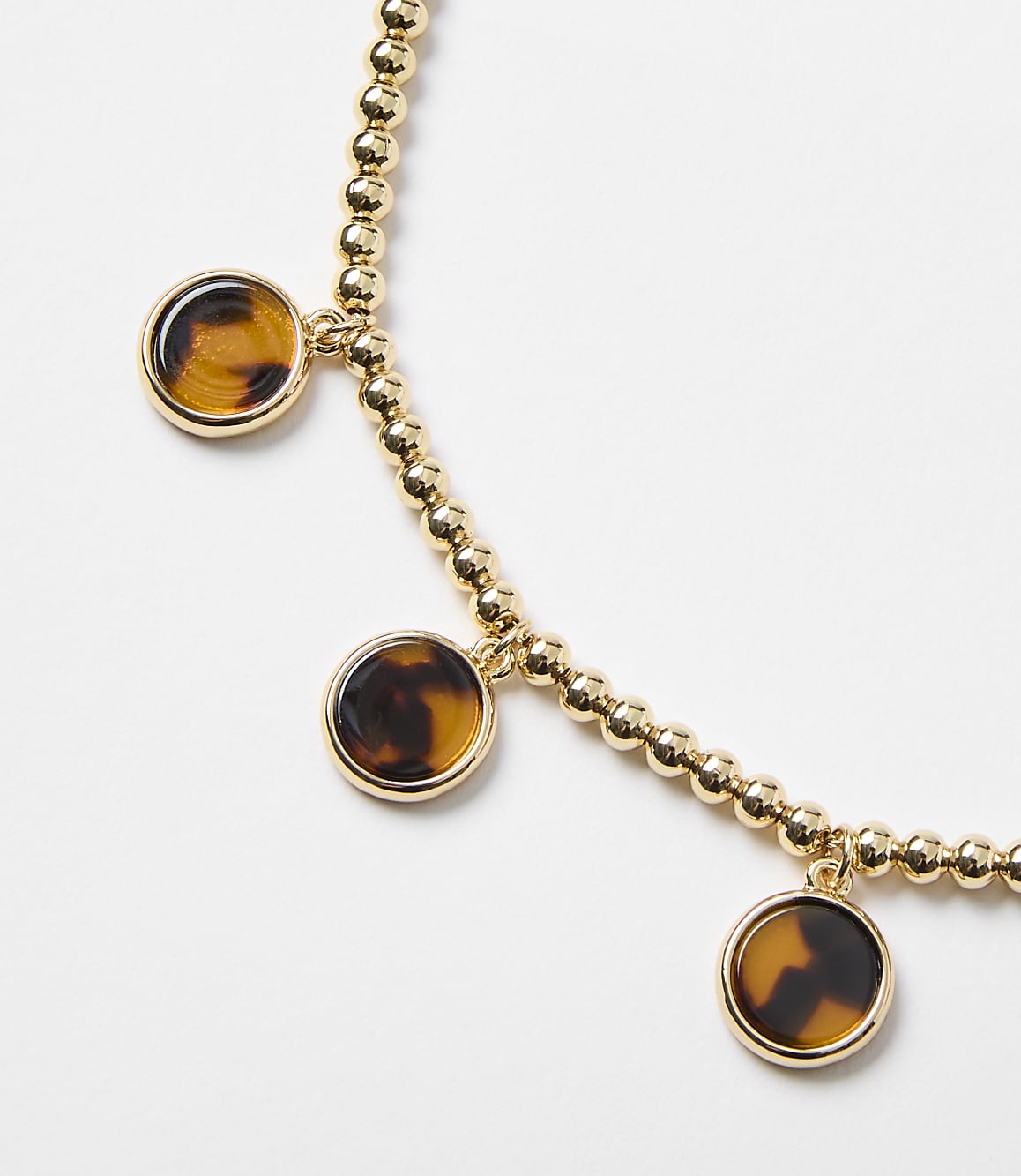 A gold beaded bracelet with three tortoise shell charms hangs against a plain white background.