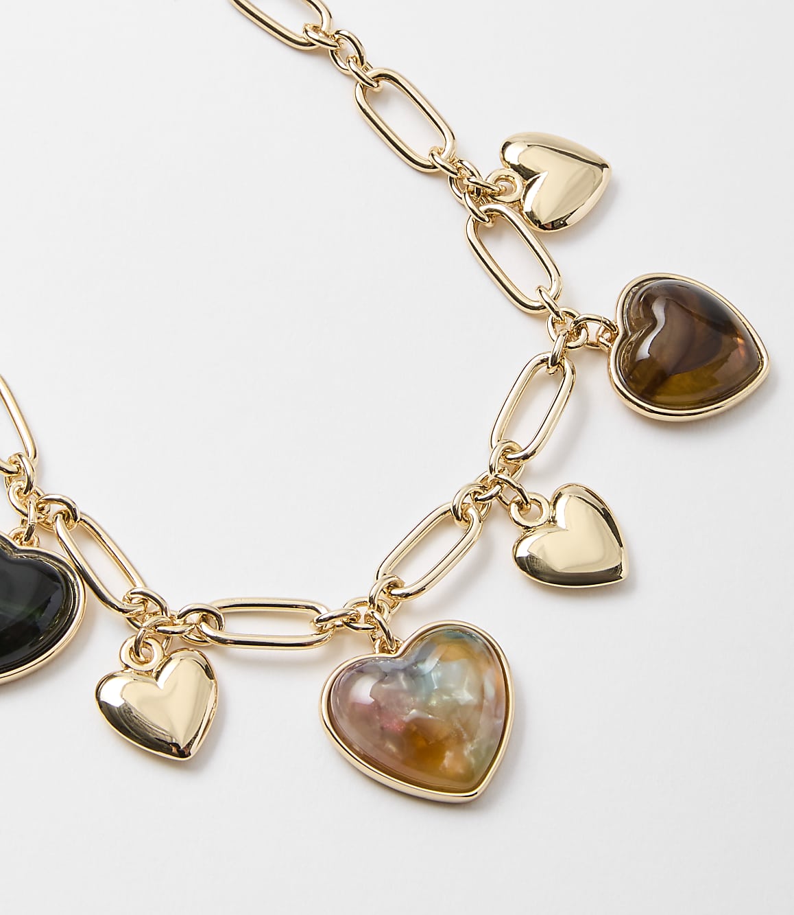 A gold chain necklace with heart-shaped charms, some made of polished stone and others of gold, rests against a plain white background.