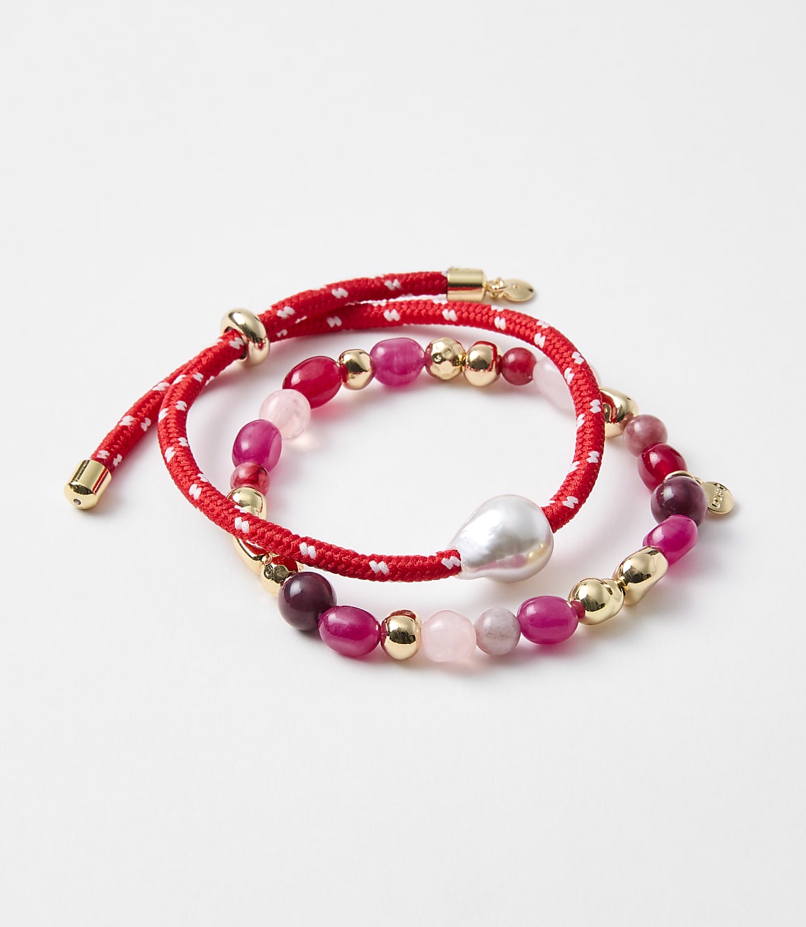 Two red beaded bracelets with gold accents and a pearl are arranged on a white background.
