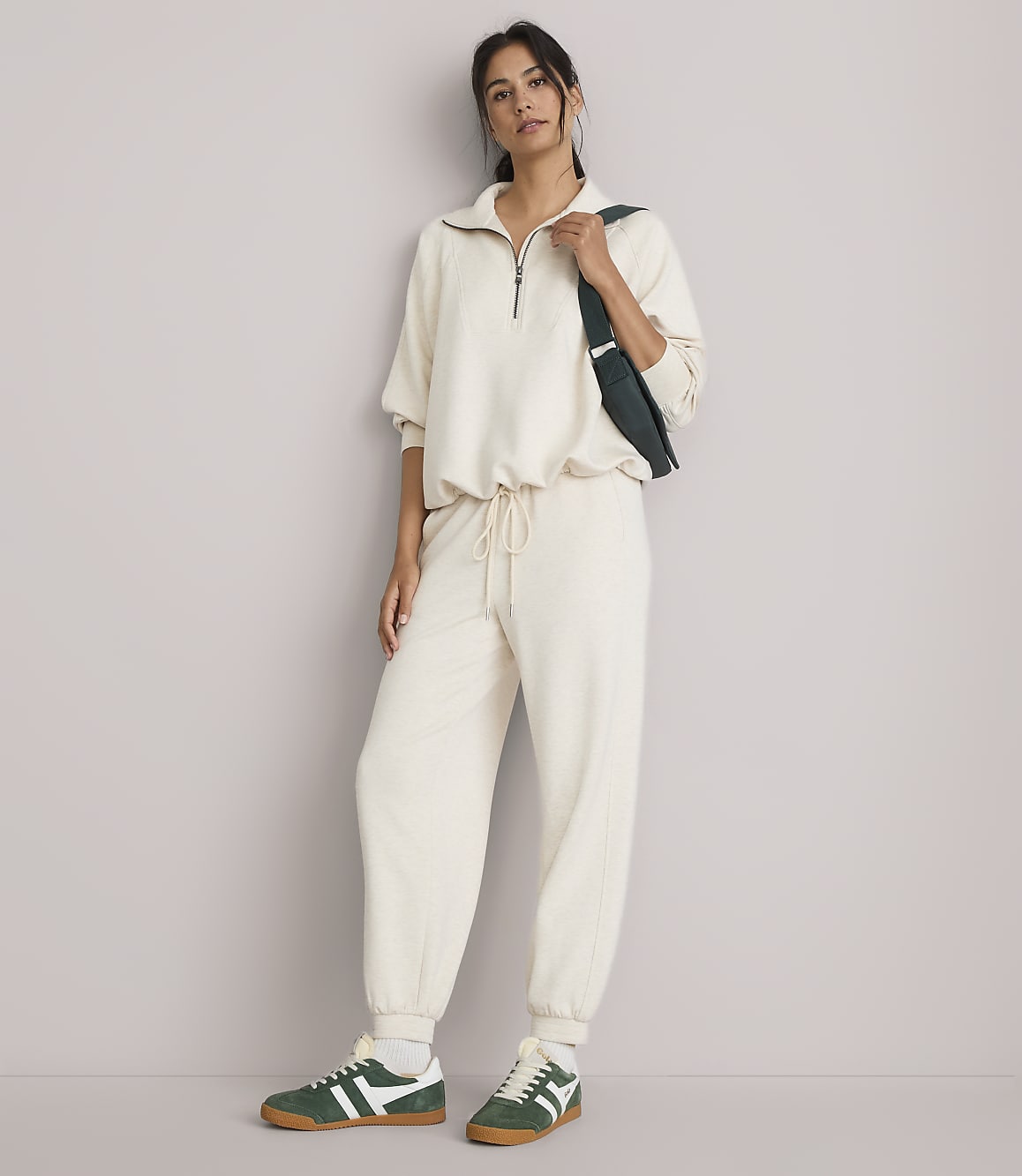 A woman in a cream loungewear set and green sneakers stands against a plain, light gray background.