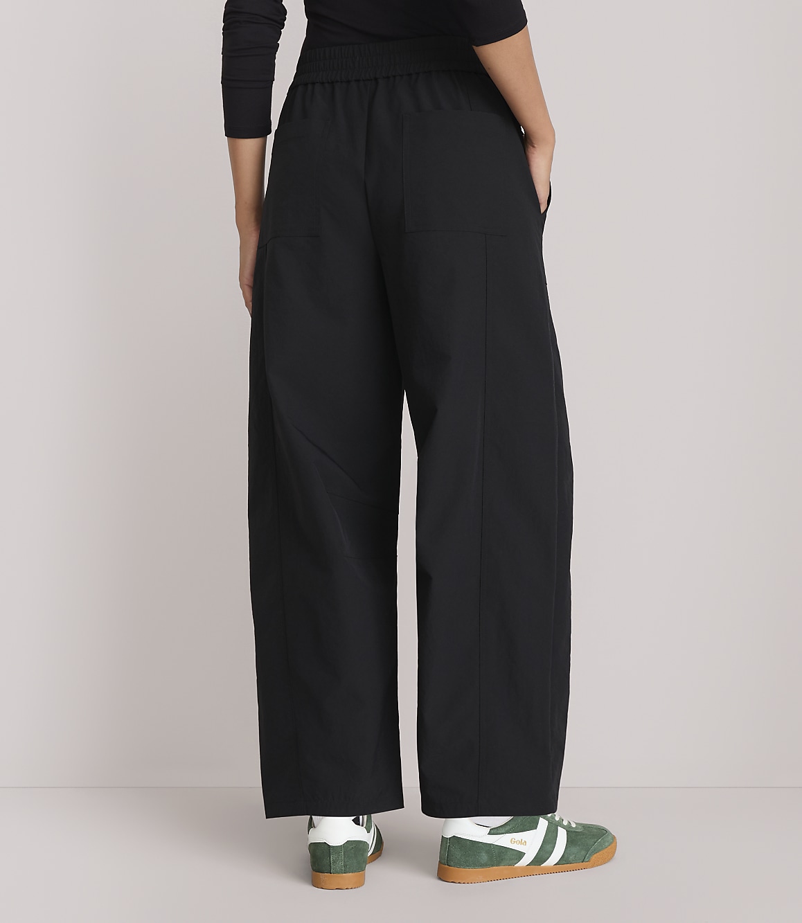 A person wearing black wide-leg pants and green sneakers stands against a plain, light gray background.