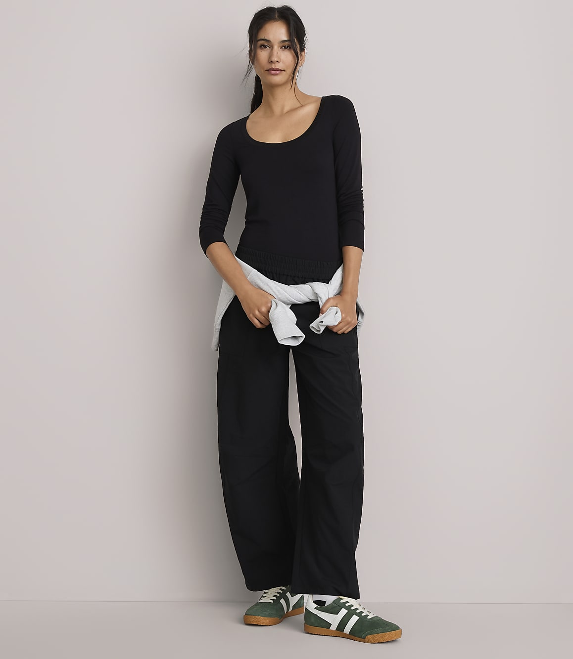 A woman in a black top and wide-leg pants stands against a plain, light-colored wall.