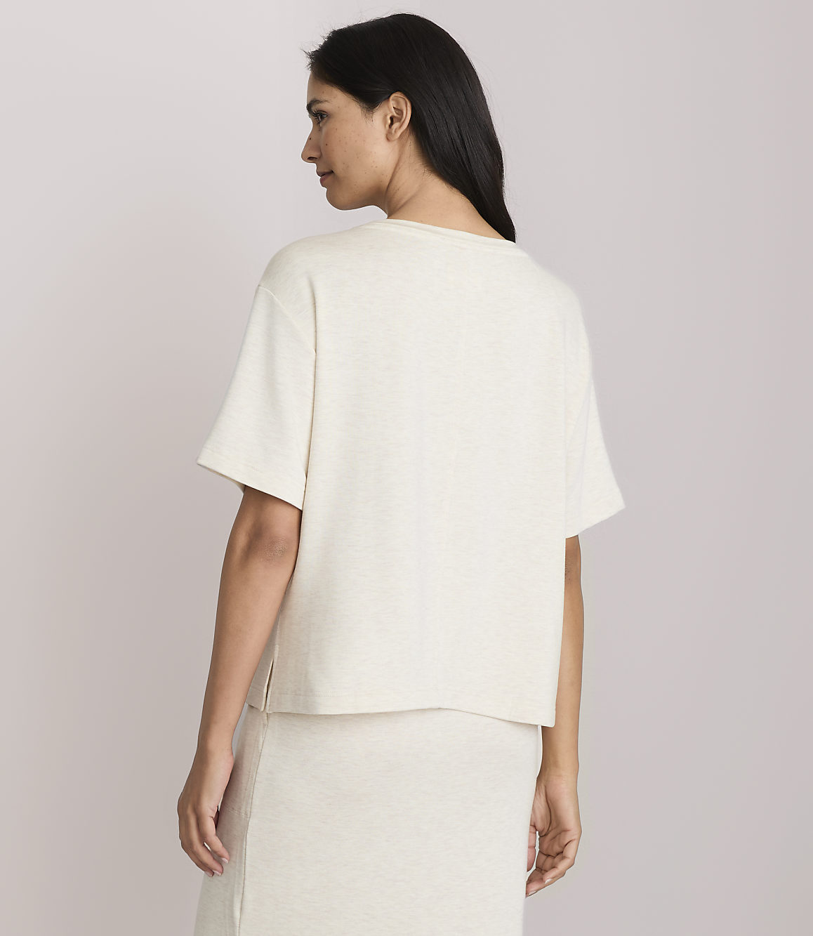 A woman in a cream-colored t-shirt and skirt stands against a plain, light-colored background.