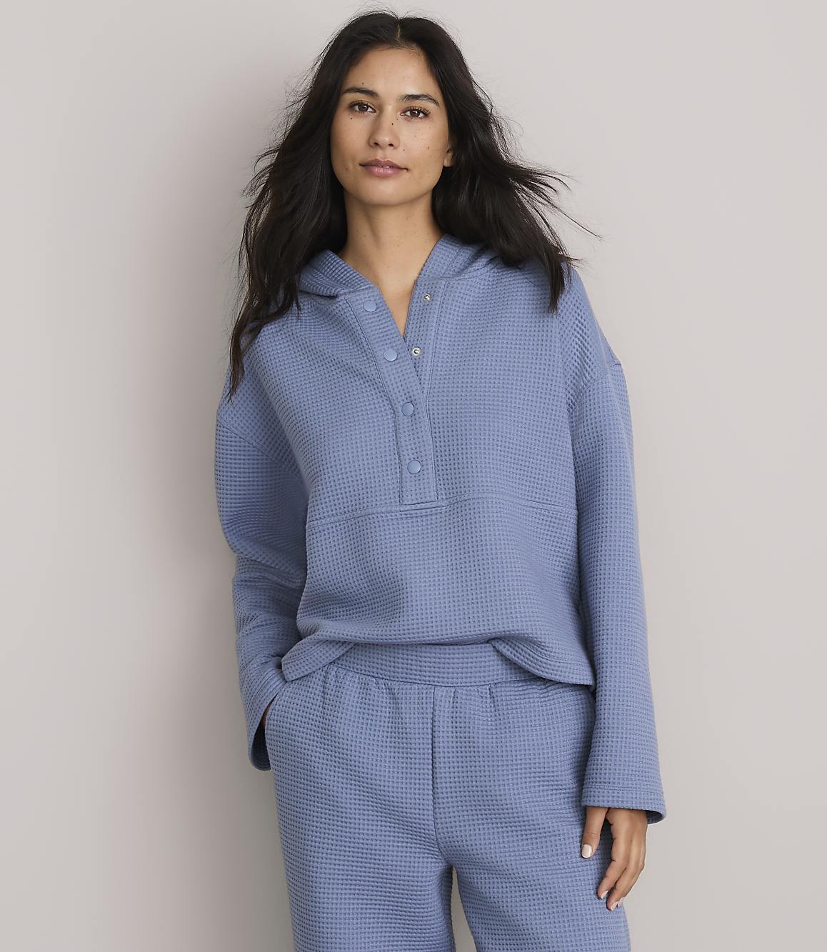 A woman in a blue waffle-knit hoodie and matching shorts stands against a plain gray background.