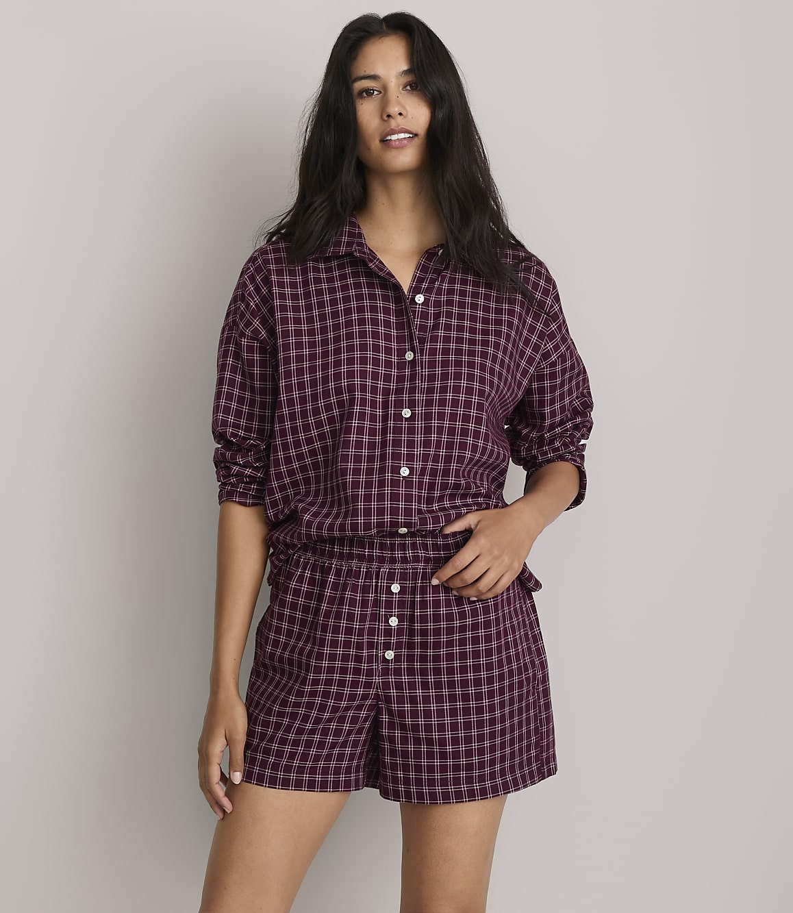 A woman in a purple gingham pajama set stands against a plain gray background.