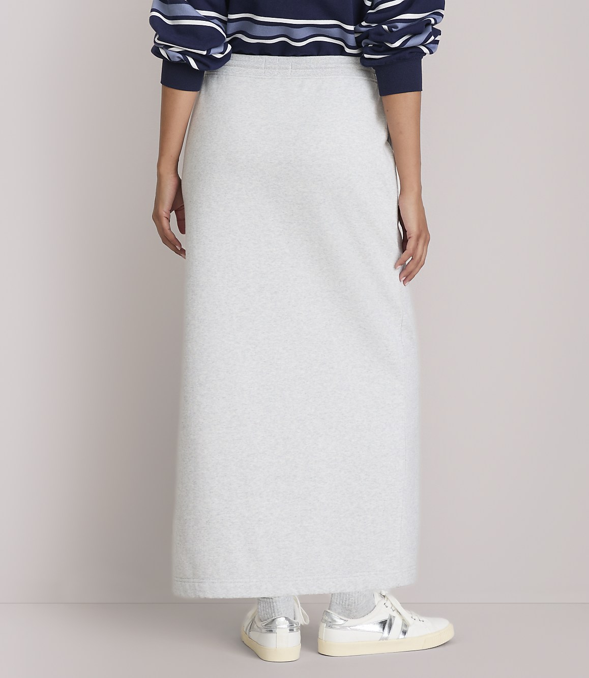 A person wearing a light gray maxi skirt and a striped sweater stands against a plain background.
