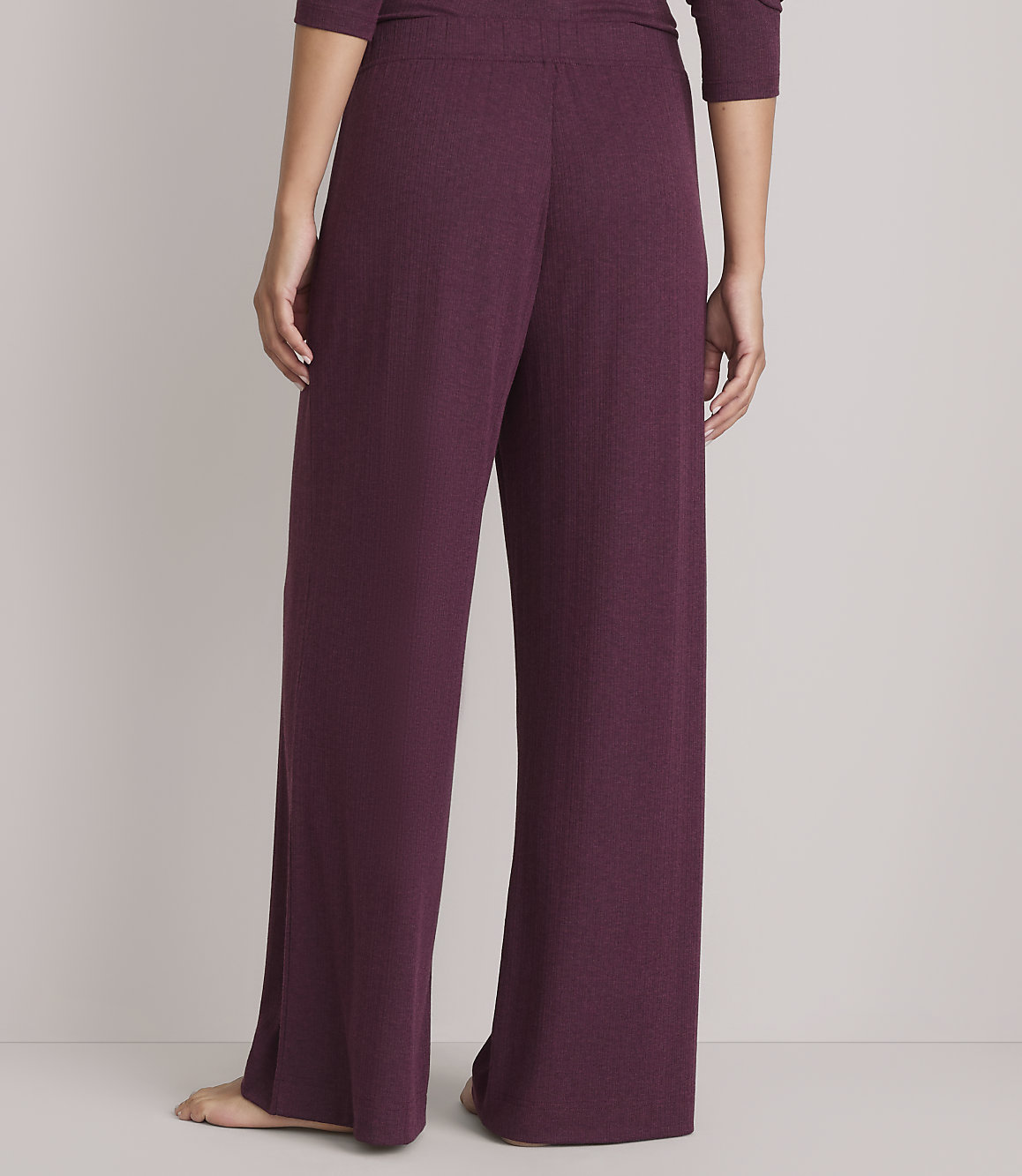 A person wearing plum-colored wide-leg pajama pants stands against a plain gray background.
