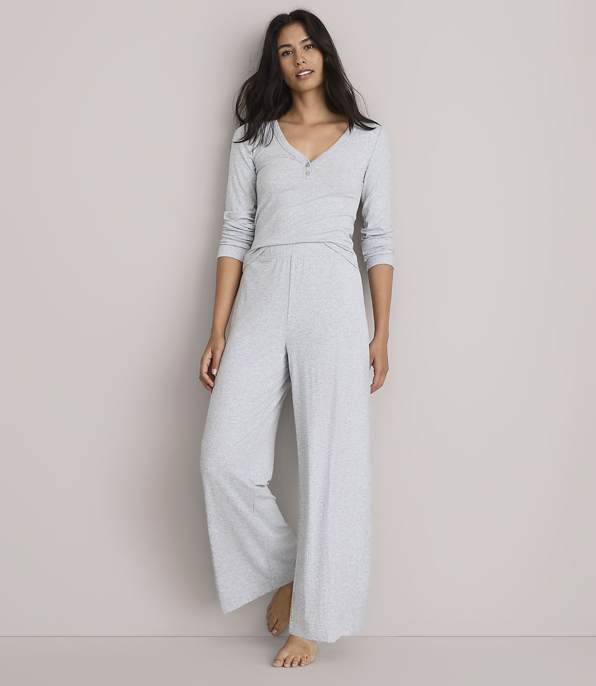 A woman in light gray pajamas stands against a plain, light gray background.