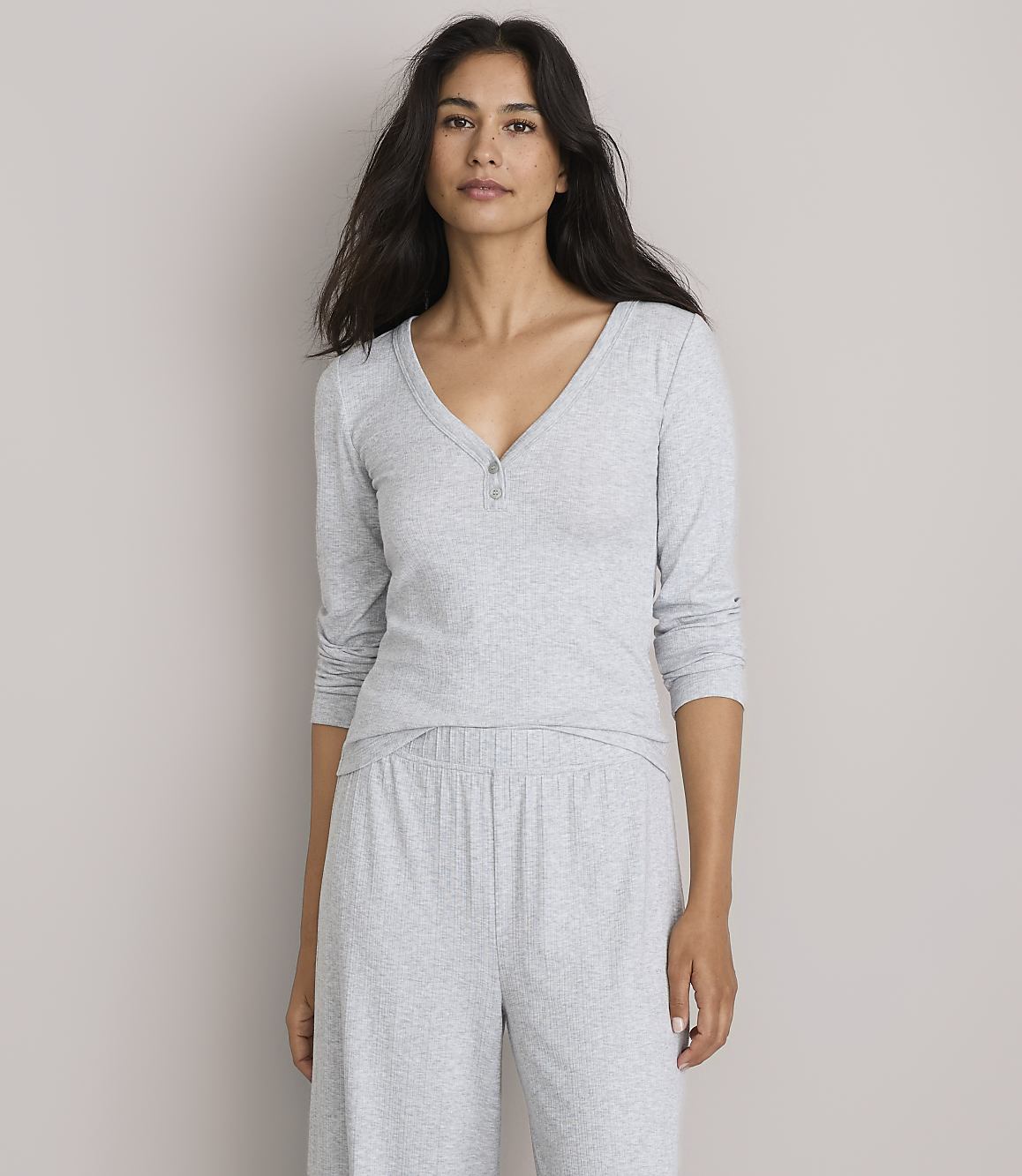 A woman in a grey pajama set stands against a plain, light grey background.