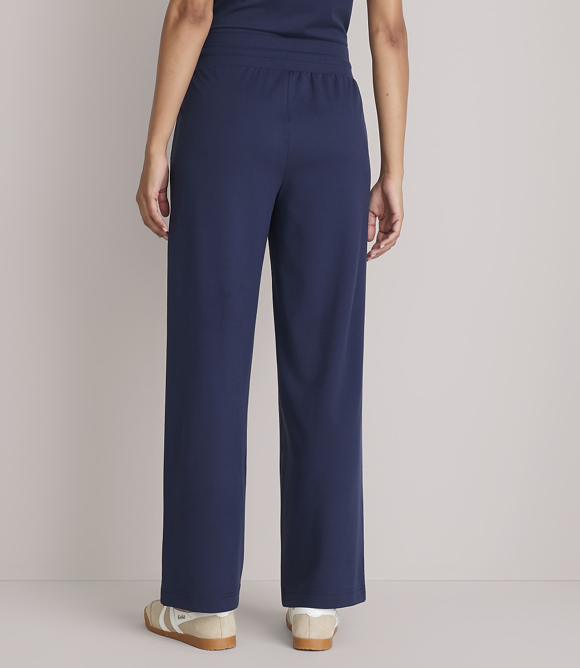 A person wearing navy blue pajama pants and sneakers stands against a plain gray background.