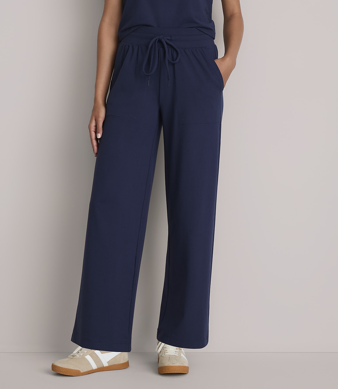 A person stands in navy blue wide-leg pants and sneakers against a plain gray background.