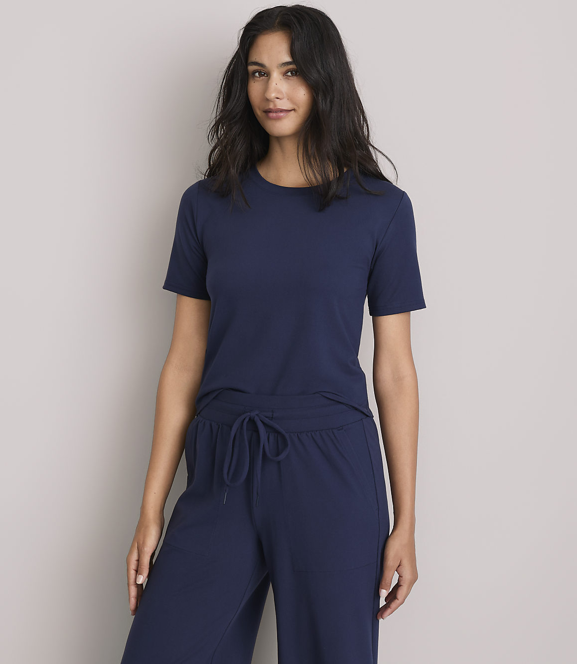 A woman in a navy blue t-shirt and matching pants stands against a plain gray background.