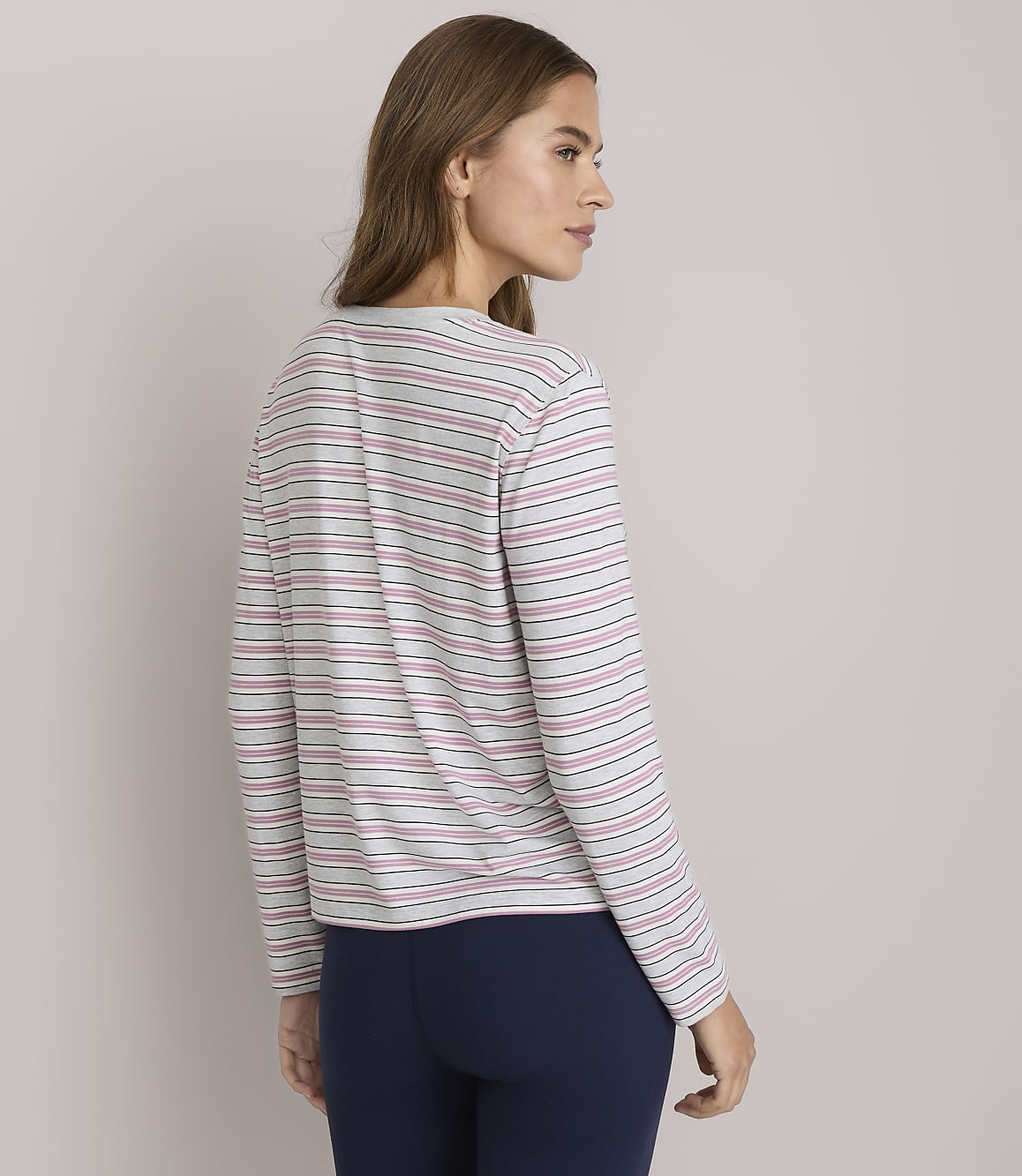 A woman in a striped shirt and navy pants stands against a plain white background.