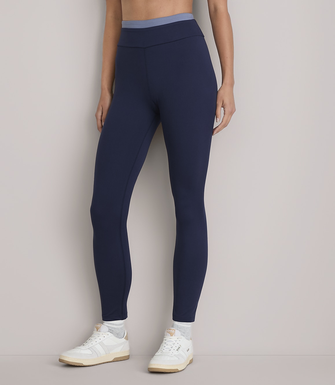 A person stands in dark blue leggings and white sneakers against a plain white background.
