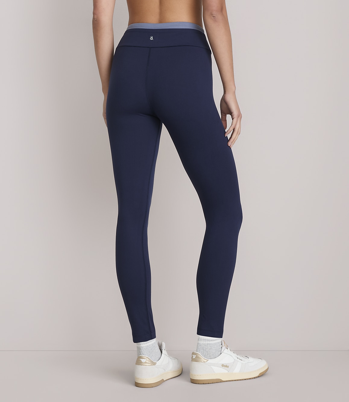 A person wearing navy blue leggings and white sneakers stands against a plain white background.