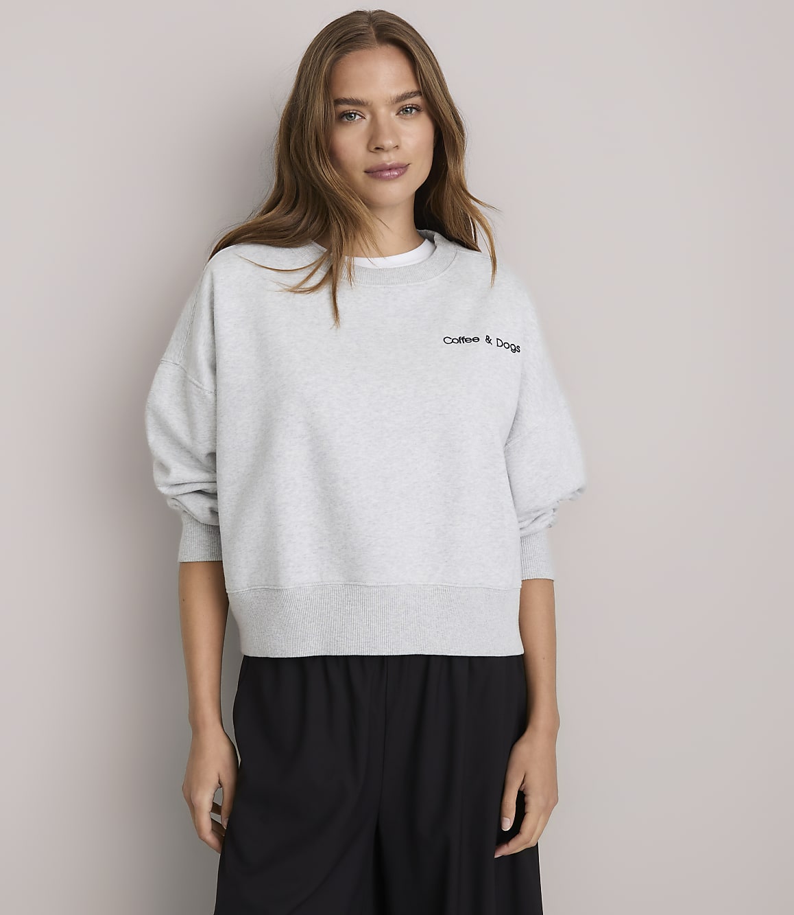 A young woman in a light gray sweatshirt stands against a plain white background.
