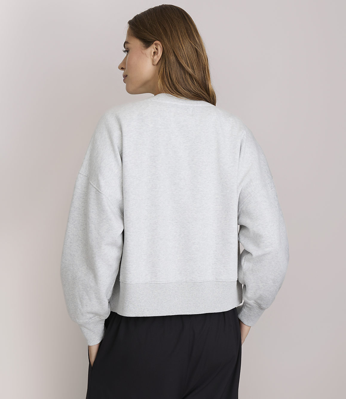 A woman in a grey sweatshirt and black pants stands against a plain white background.