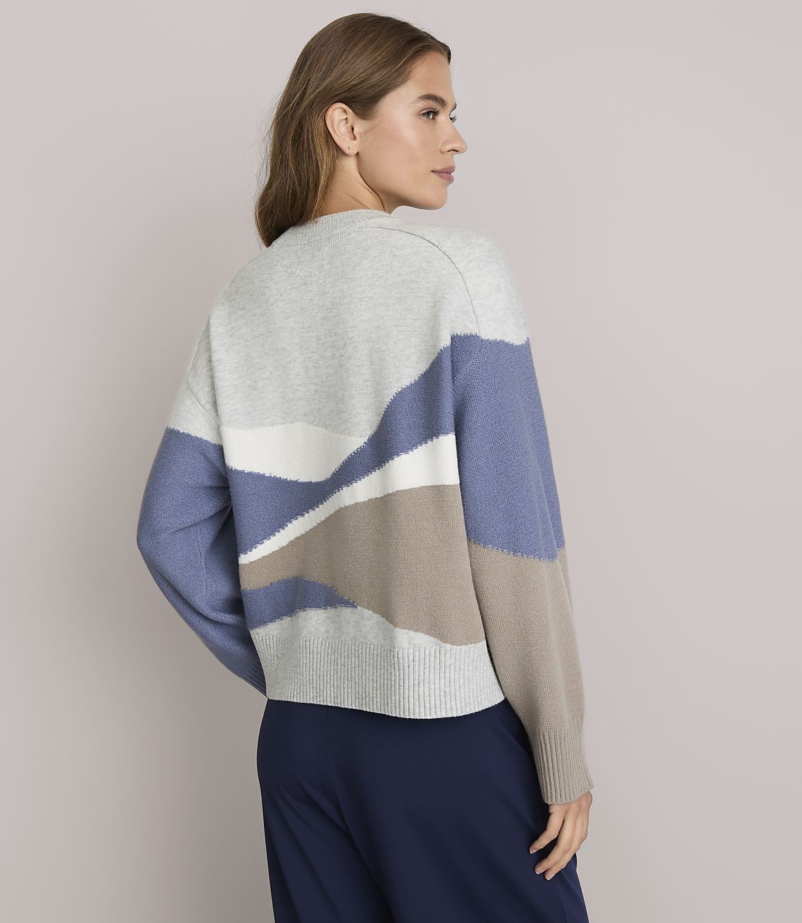A woman in a patterned sweater stands against a plain background.