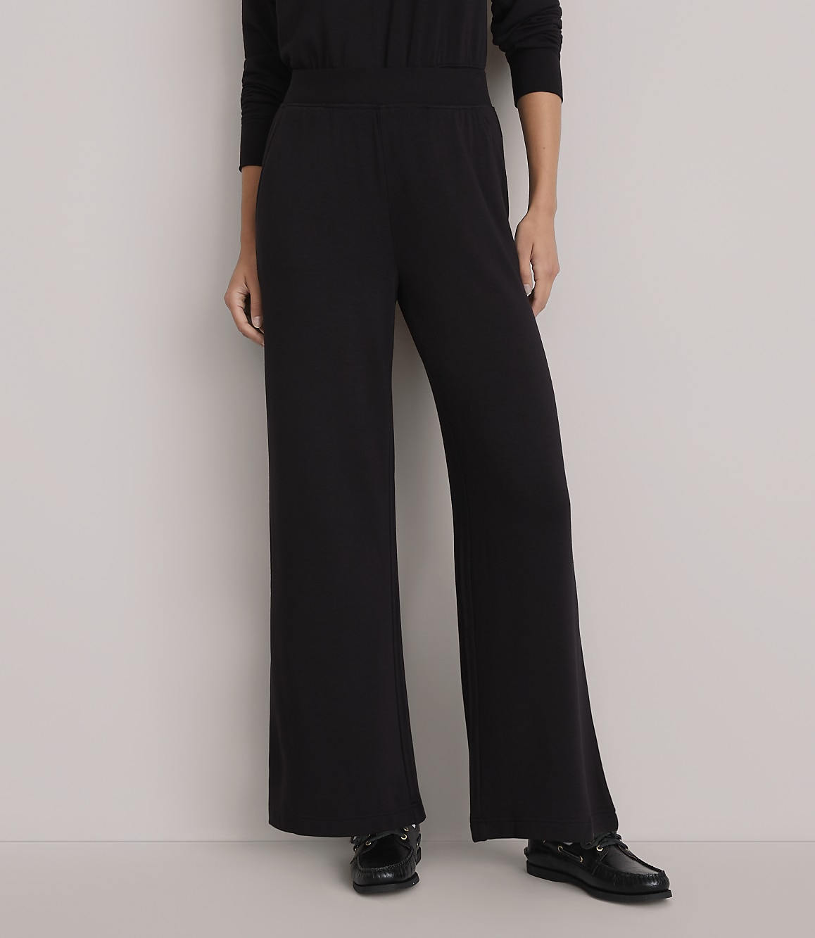 A person stands in wide-legged black pants and black shoes against a plain white background.