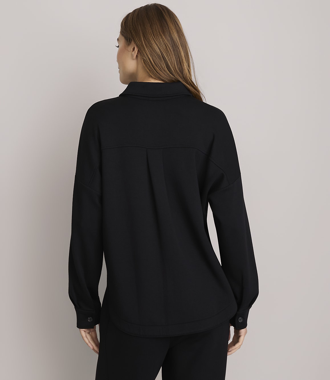 A woman in a black shirt and pants stands against a plain white background.