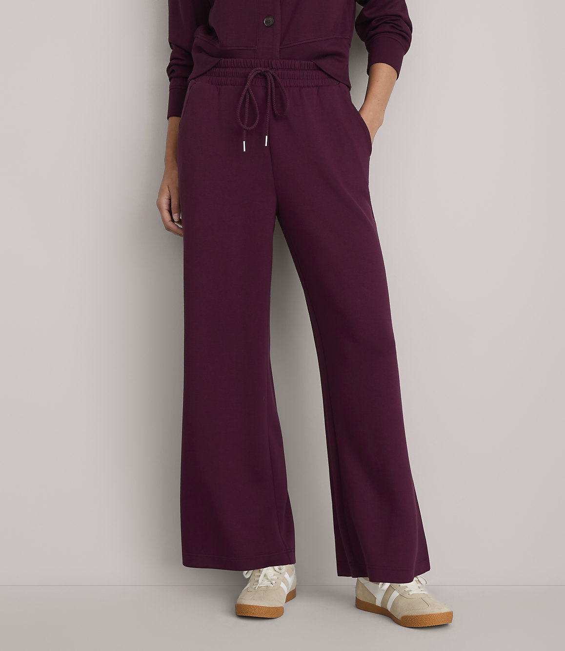 A person wearing burgundy wide-leg sweatpants and sneakers stands against a plain white background.