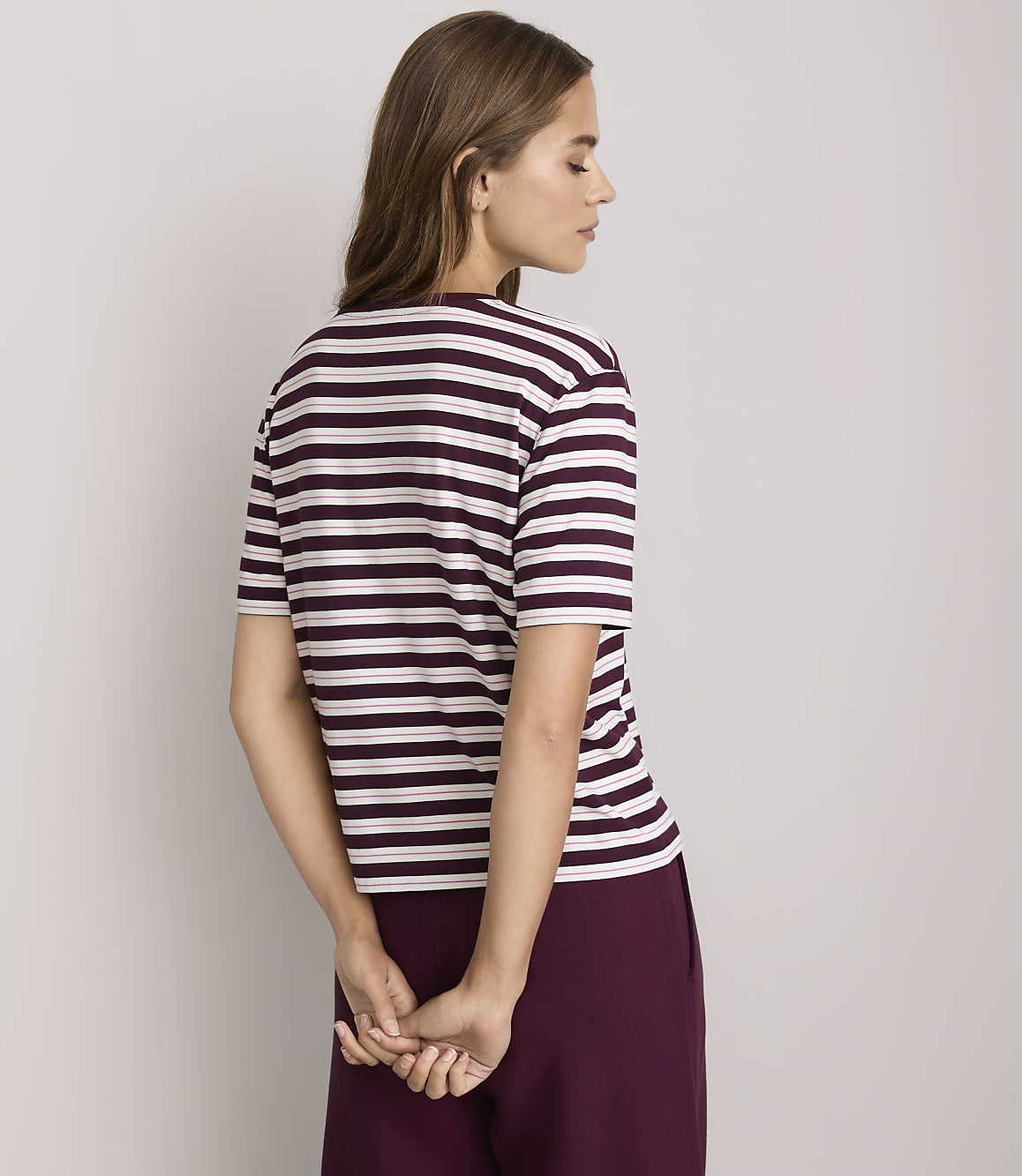 A woman in a striped t-shirt and maroon pants stands against a plain white background.