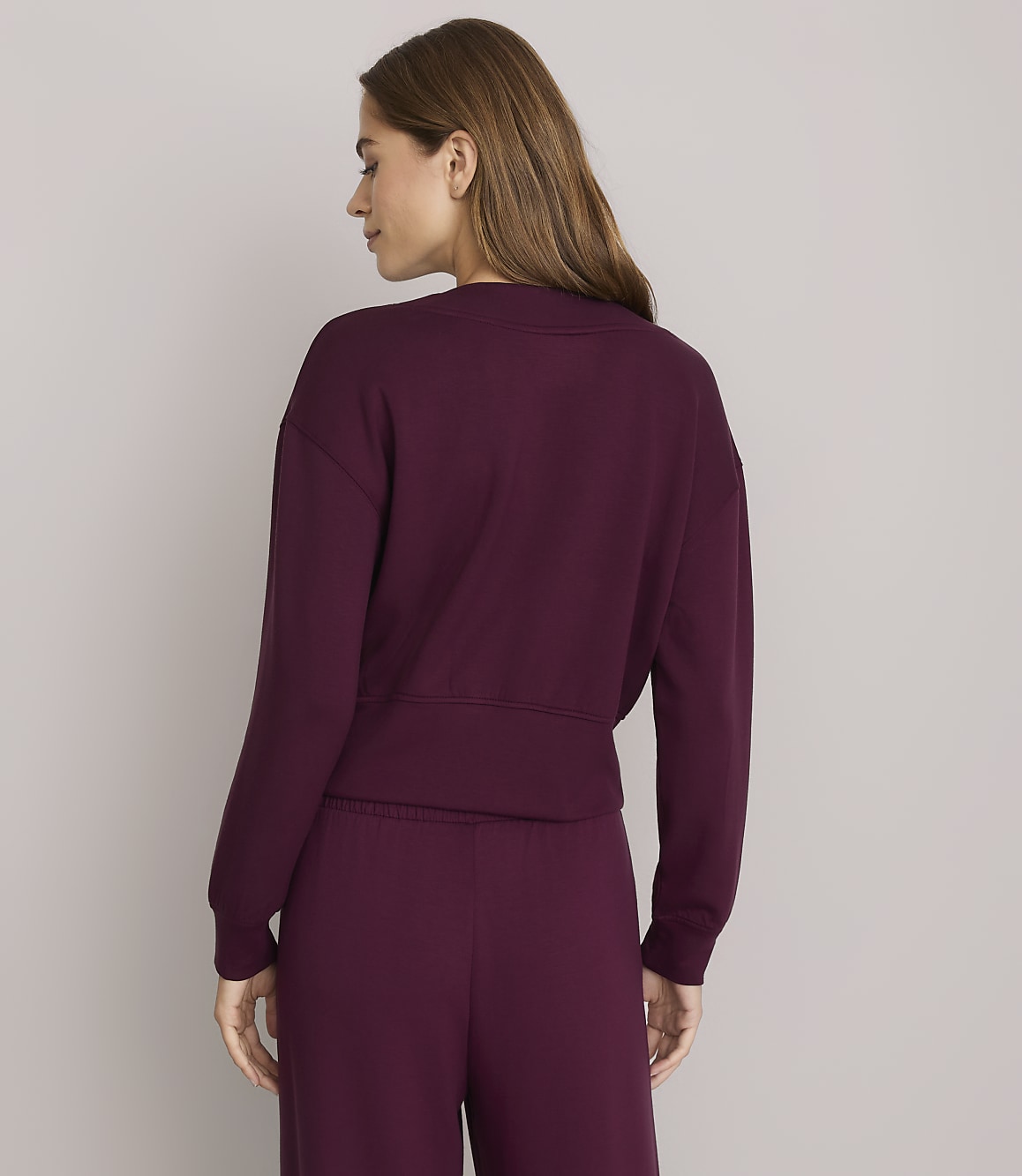 A woman in a burgundy sweatshirt and pants stands against a plain gray background.