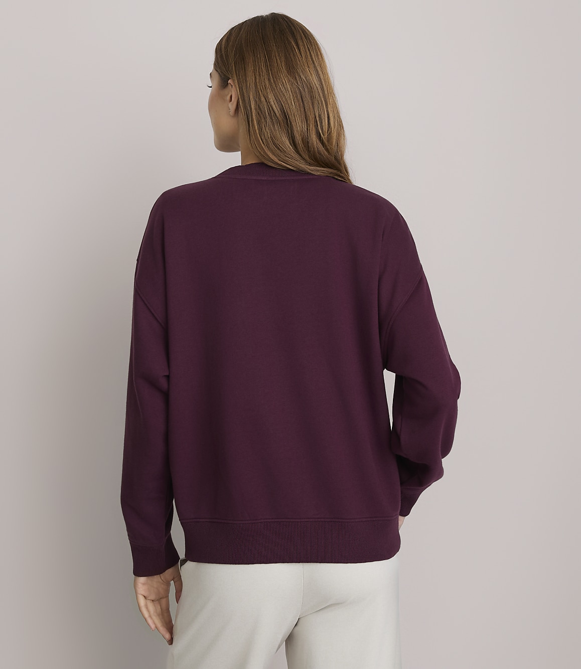 A woman in a maroon sweatshirt stands against a plain, light gray background.