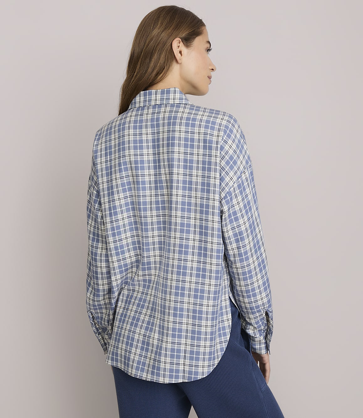 A woman in a blue plaid shirt stands against a plain white background.