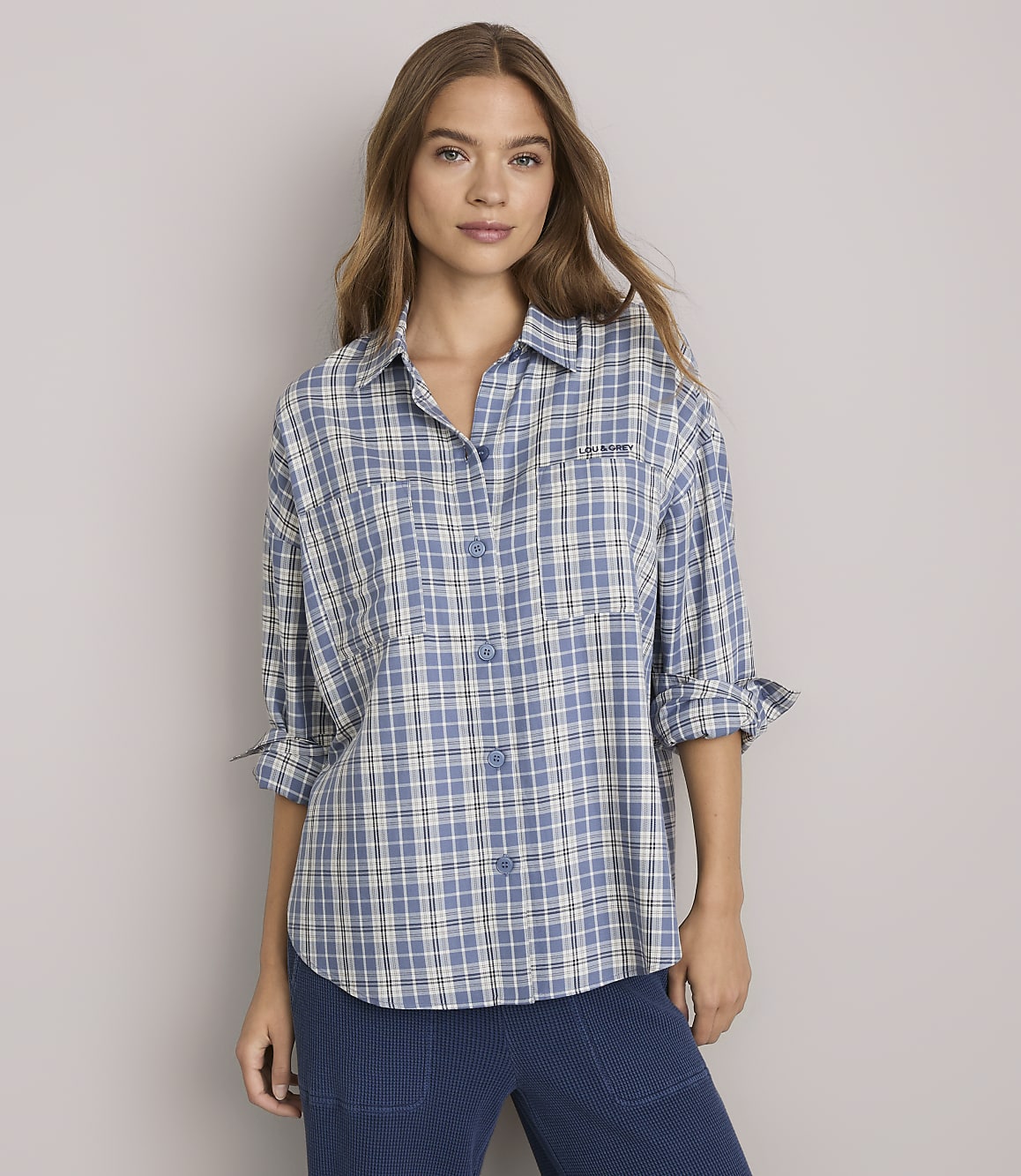 A woman in a blue plaid shirt stands against a plain gray background.