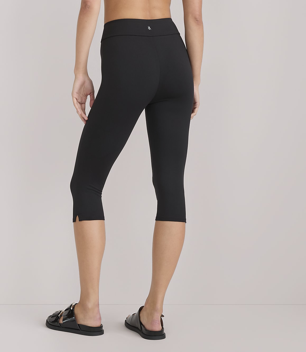 A person wearing black capri leggings and sandals stands against a plain white background.