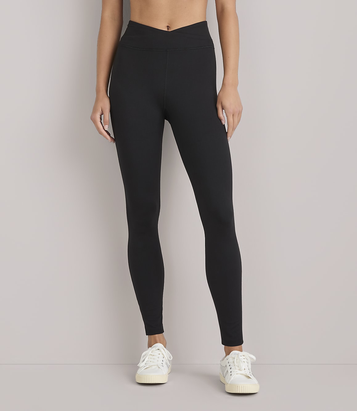 A woman wearing black leggings and white sneakers stands against a plain white background.